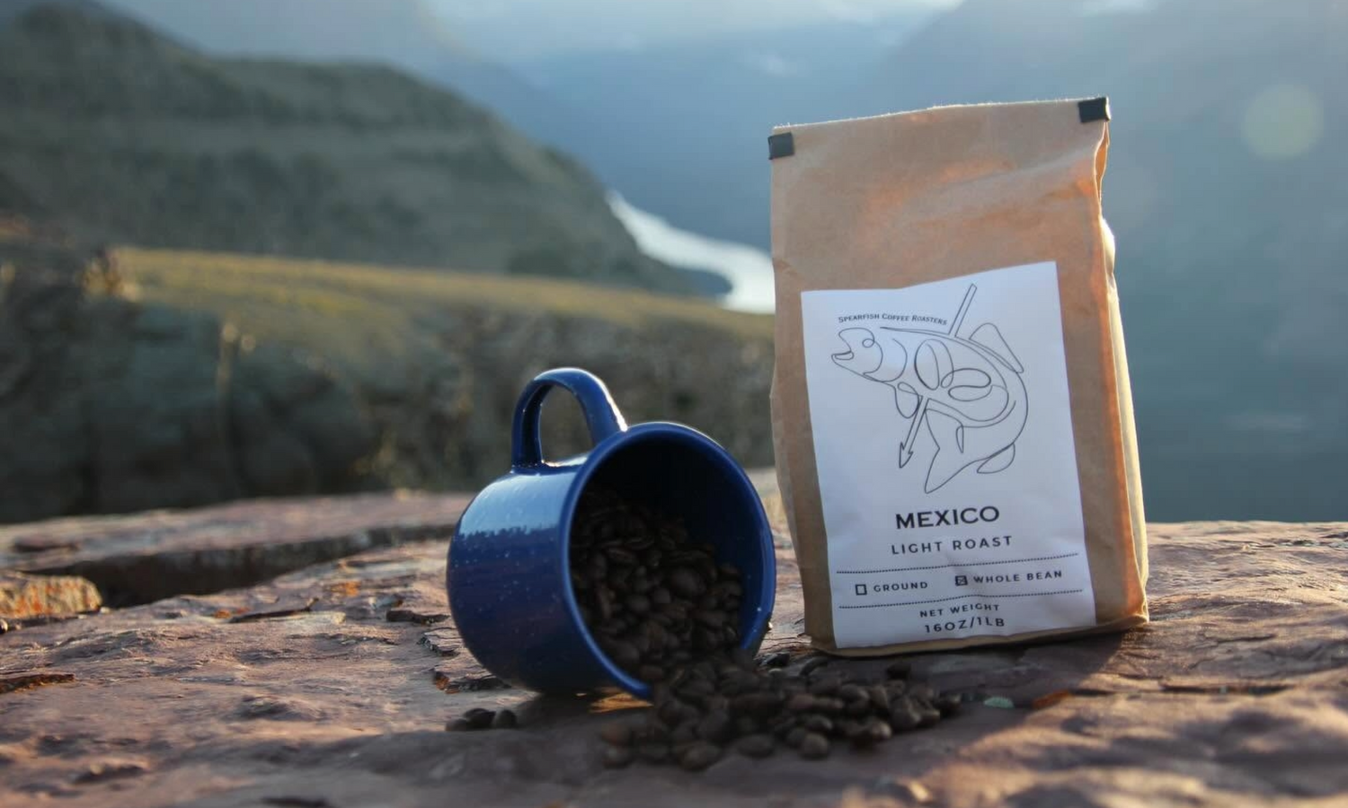 Spearfish Coffee Roasters Mexico Light Roast Whole Bean Coffee Next to Enamel Mug with Beans Spilling Out